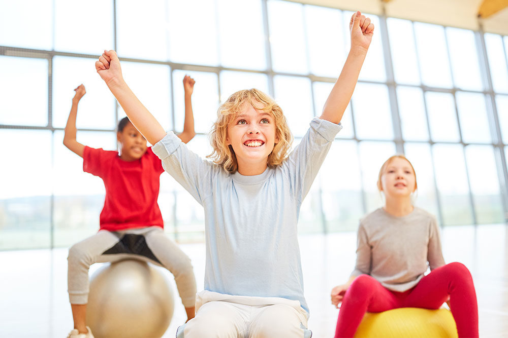 Drei junge Kinder sitzen motiviert auf einem Gymnastikball